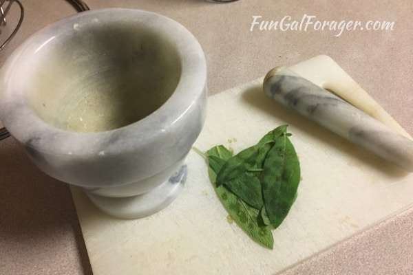 green sage leaves next to marble mortar and pestle