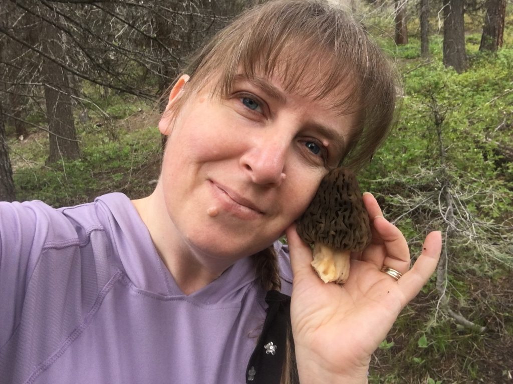 FunGal Forager in lavender shirt holding morel mushroom